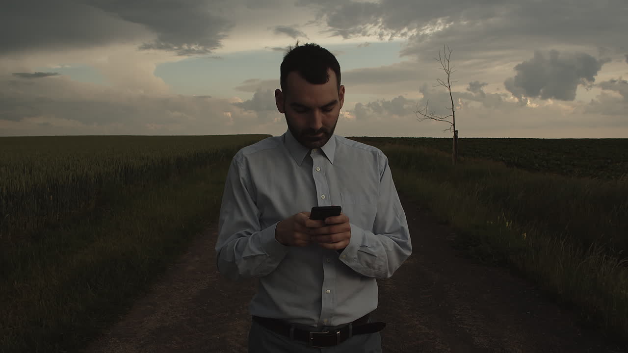Manager che usa il cellulare all'aperto in mezzo ai campi e scatta una foto, vista frontale