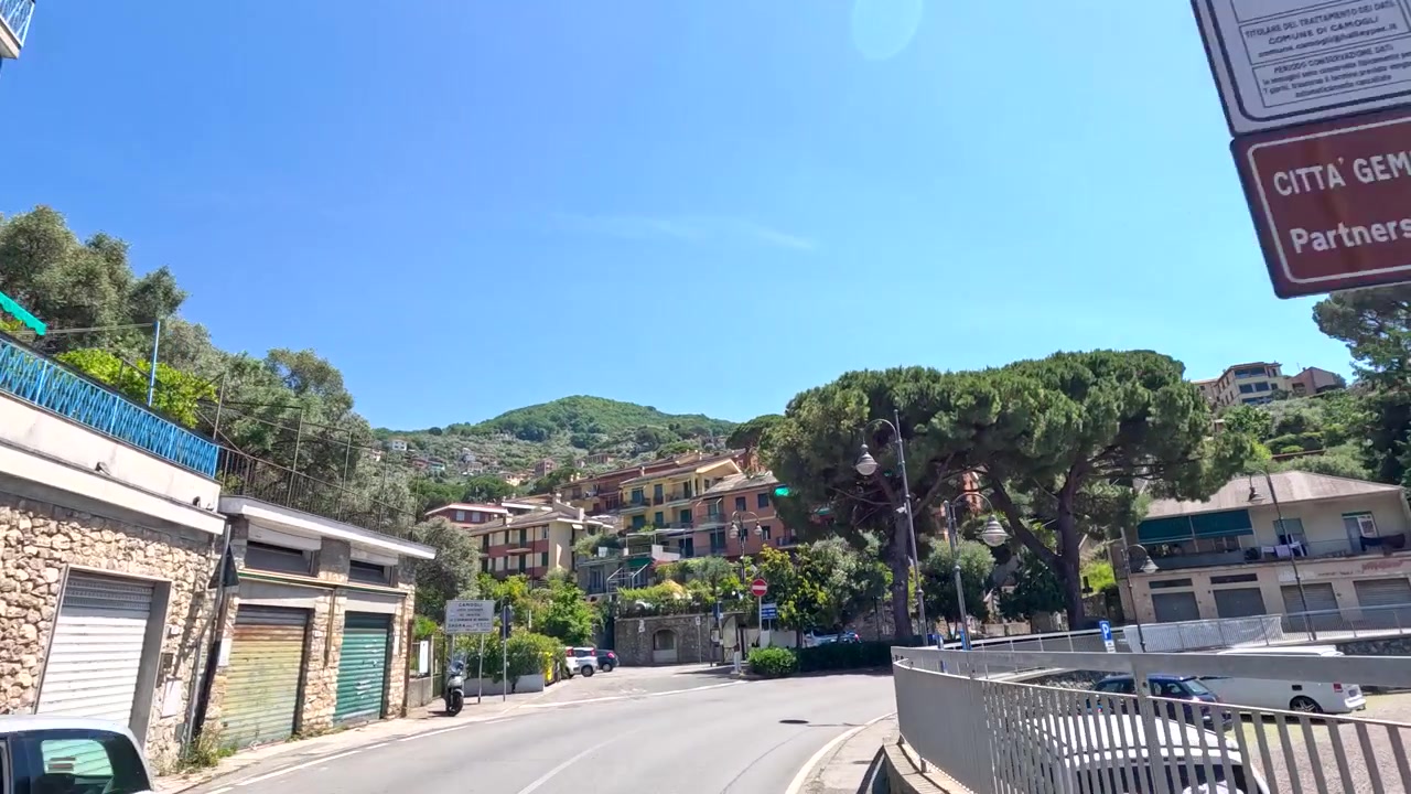 Una ripresa in prima persona da un veicolo che viaggia lungo una strada assolata, passando accanto a colorati edifici italiani.
