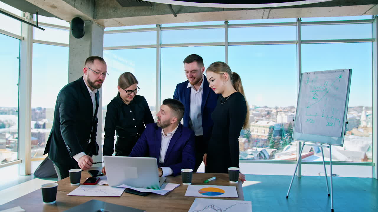 Teamwork of business people. Group of young entrepreneurs men and women use laptop and talk together in modern office. Panoramic window view with a city background.