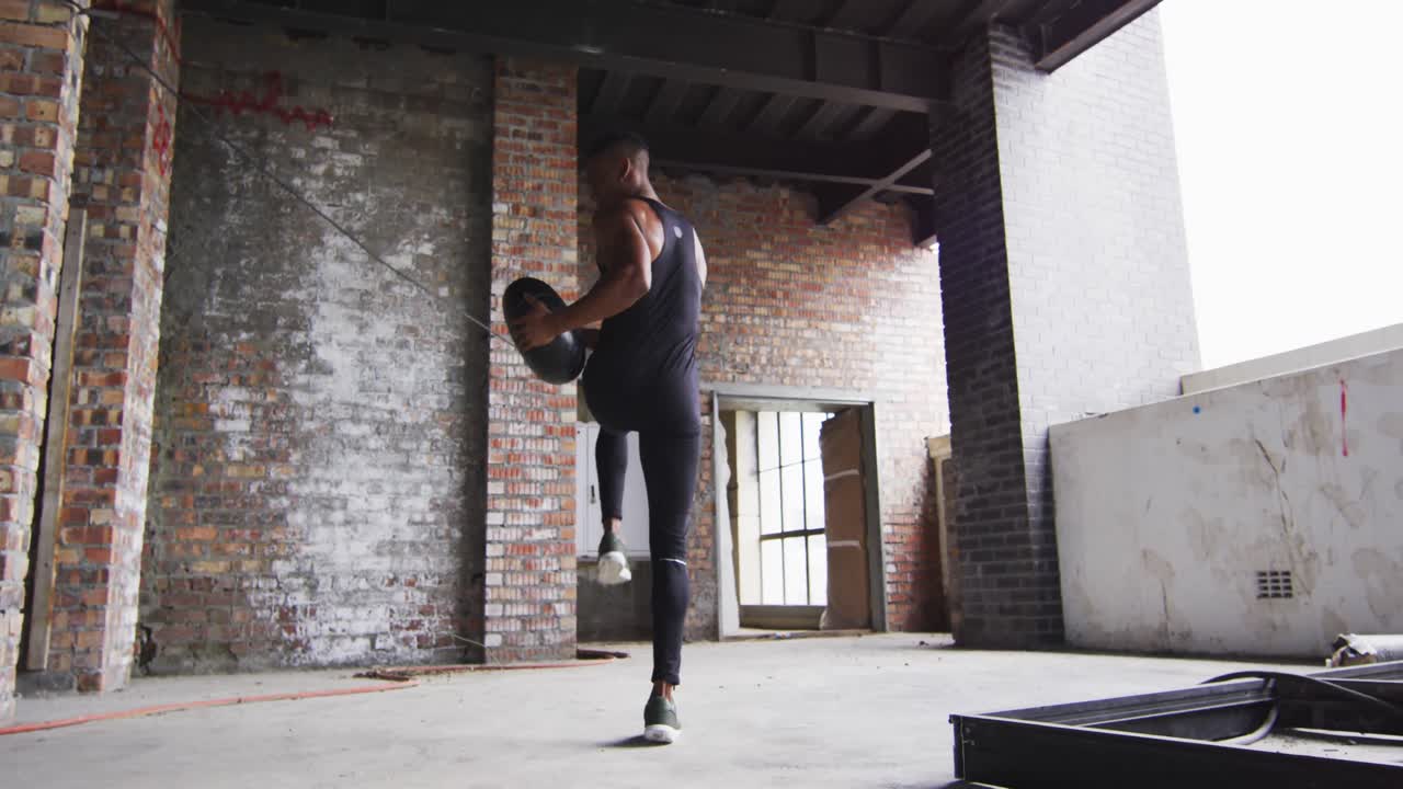 빈 도시 건물에서 의학 공으로 운동하는 아프리카계 미국인