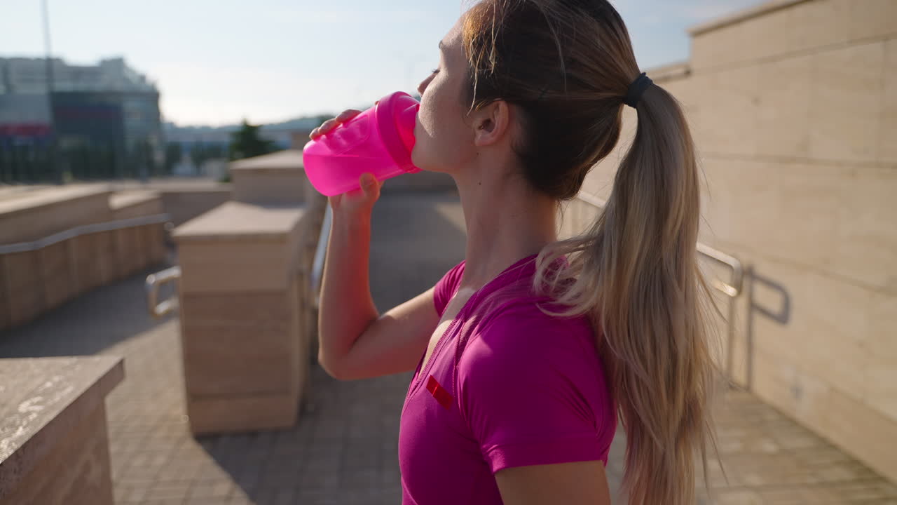 mujer bebiendo agua después de una carrera en la ciudad