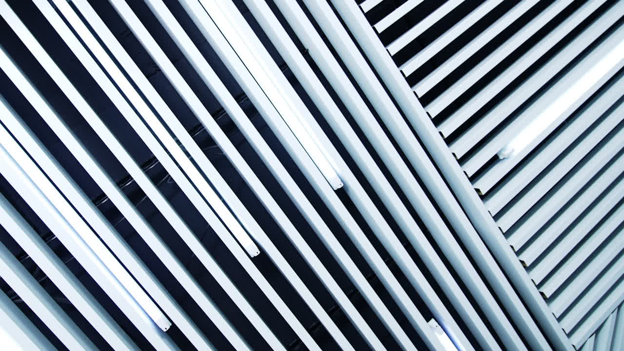 Long lamps of daylight on the ceiling. White planks parallel to the illumination equipment.