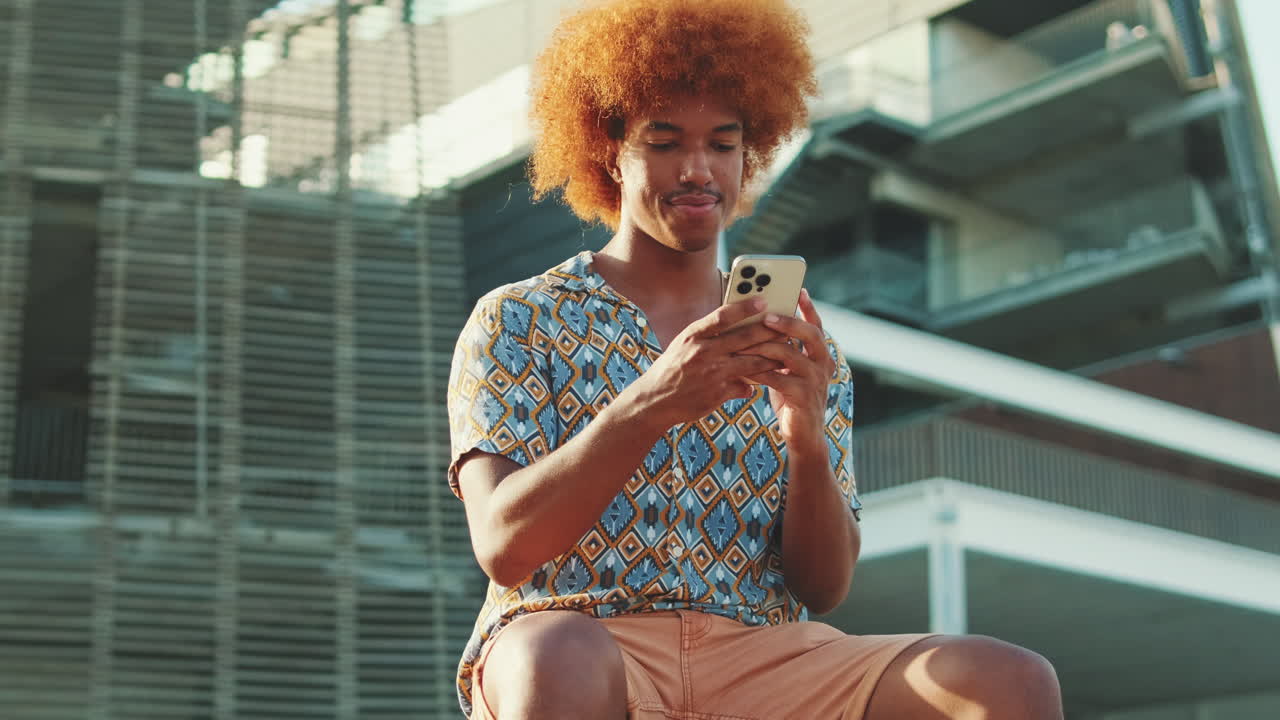 Ung mand med krøllet, rødt hår bruger smartphone udendørs