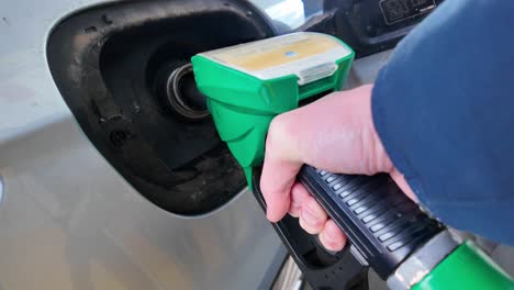 hand holding pump nozzle at gas station, filling car tank with fuel