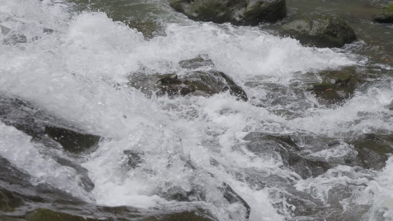 Close-up of bubbling water cascading over the rocks of Goa Rang Reng Waterfall in Bali, Indonesia, captured in slow motion