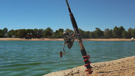 cierre en cámara lenta de la caña de pescar fijada en la arena por el lago ondulante en california
