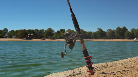 slow motion close up of fishing rod fixed in sand by rippling lake in california