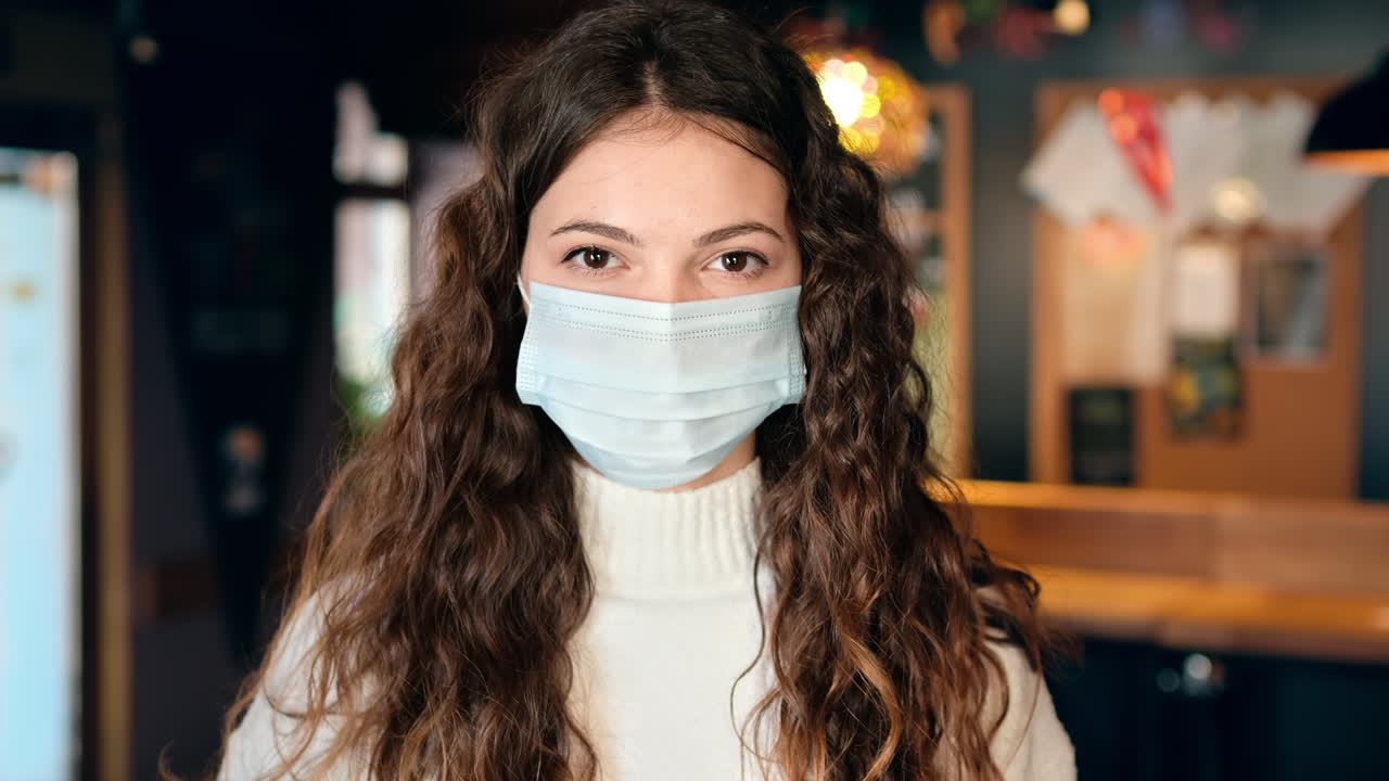 Mujer con mascarilla médica mostrando un smartphone con el Certificado Internacional de Vacunación COVID-19 en una cafetería. Dosis de refuerzo, interior de la cafetería