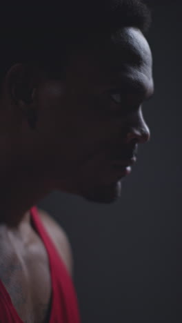 vertical video close up profile shot of determined male boxer or athlete training in gym preparing for fight or sports event against black studio background