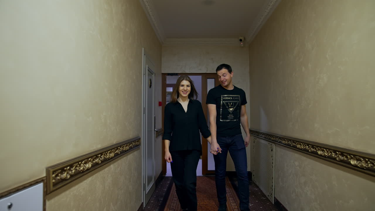 Couple walking by the corridor holding by the hands and talking. Man and woman go indoors by the long hall.
