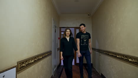 couple walking by the corridor holding by the hands and talking. man and woman go indoors by the long hall.