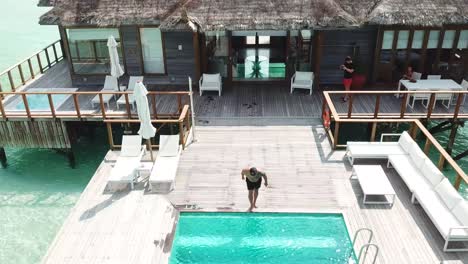 aerial, reverse, drone shot, away from a man jumping in a pool, at a villa, in middle of swallow, emerald sea, on a sunny day, on the conrad rangali island, in maldives