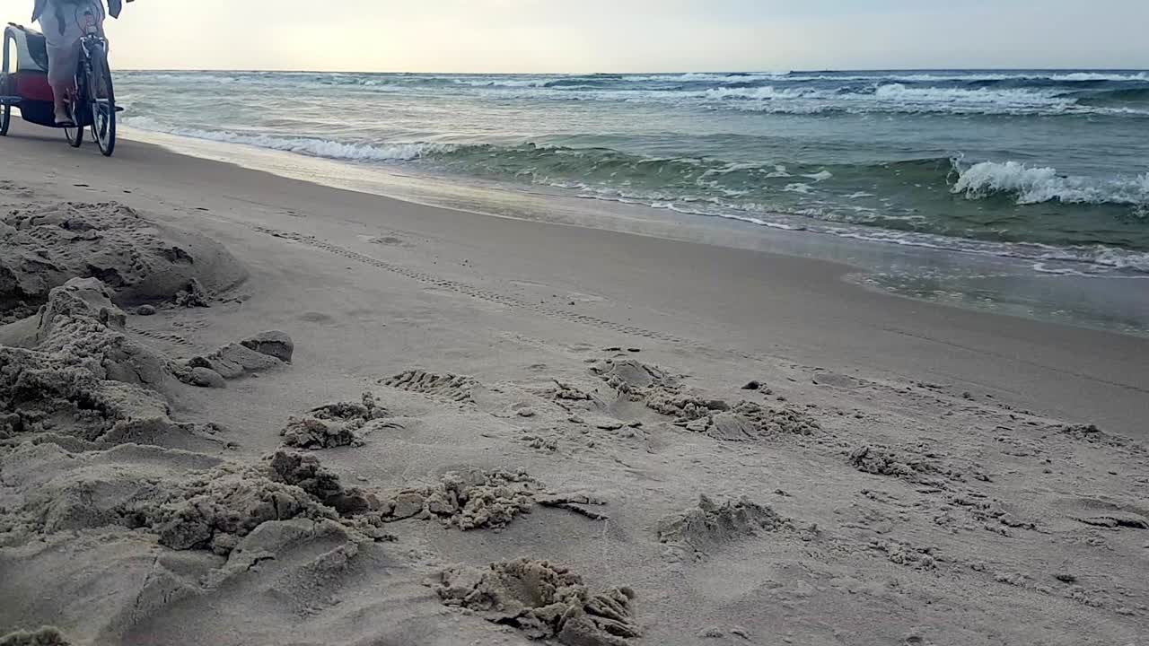 아기 트레일러와 함께 모래 해변에서 자전거를 타는 여자