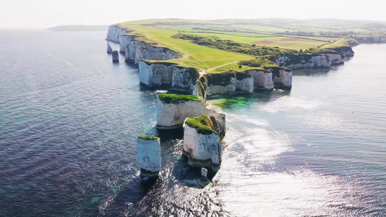 Nagranie z drona przedstawiające Old Harry Rocks na wybrzeżu Dorset w Anglii, ukazujące dramatyczne białe kredowe skały morskie, klify, turkusową wodę i zielone ścieżki na szczytach klifów. Ujęcie ukazuje słynne.