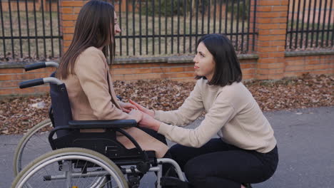 woman squatting talking with her female disable friend in wheelchair in the street