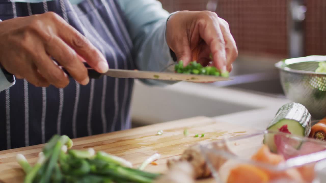 Mid section of asian senior woman putting chopped vegetables in a bowl in the kitchen
