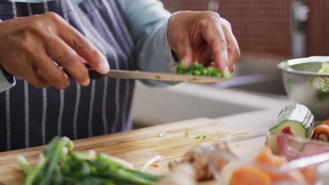 Mid-section-of-asian-senior-woman-putting-chopped-vegetables-in-a-bowl-in-the-kitchen