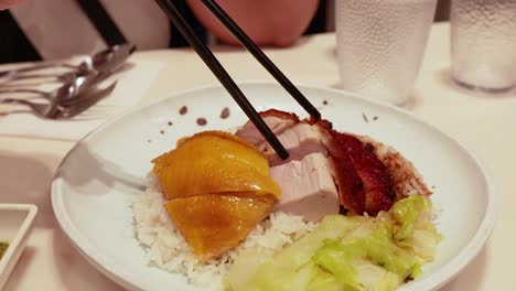 chopsticks picking roast meats from rice plate