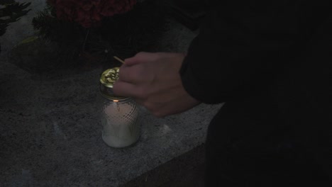 a hand lights a candle on a grave during all saints' day, symbolizing reverence and remembrance amidst the solemn atmosphere