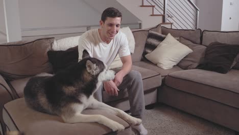 un joven le da a su adorable perro un regalo mientras se relaja en una sala de estar.