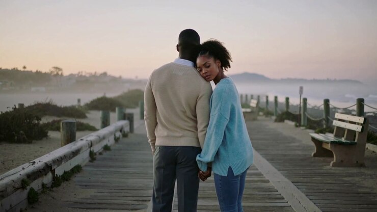 Walking pair holding on boardwalk to horizon woman turning back leaning looking right in sweaters
