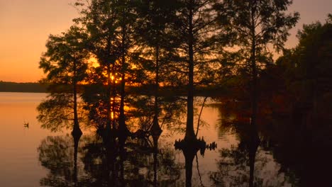 Aerial-Footage-of-a-sunset-aquatic-landscape-with-peaceful-solar-flares-radiating-through-the-silhouette-trees---A-place-of-remembrance-and-spiritual-reflections