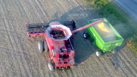 aerial drone view of the top of a red combine unloading soybeans into a green wagon about an hour before sundown