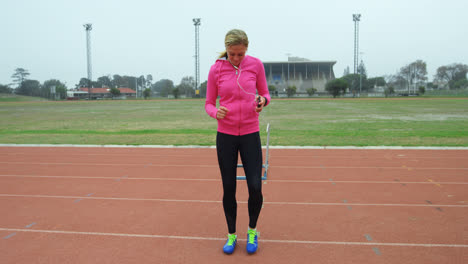 vista frontal de una atleta caucásica escuchando música en el teléfono móvil mientras hace ejercicio en la pista de carreras