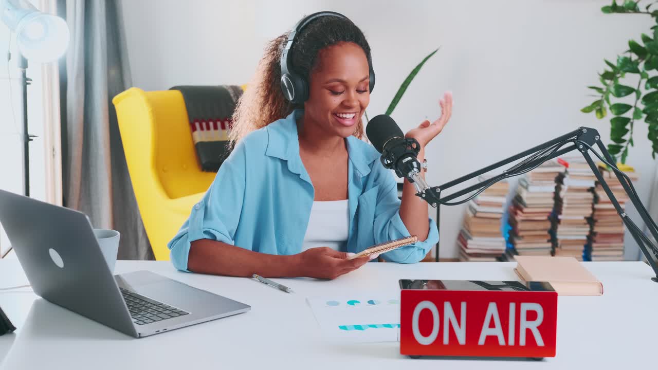 joven feliz mujer afroamericana blogger hablando en el micrófono se sienta en el escritorio