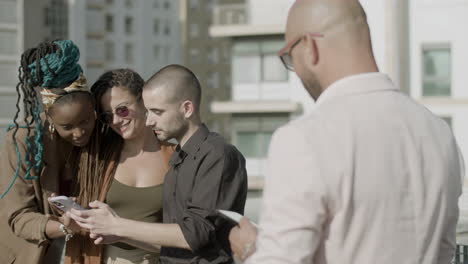 happy coworkers looking at phone screen during outdoor party