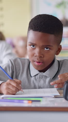 young boy writing in his notebook in a classroom