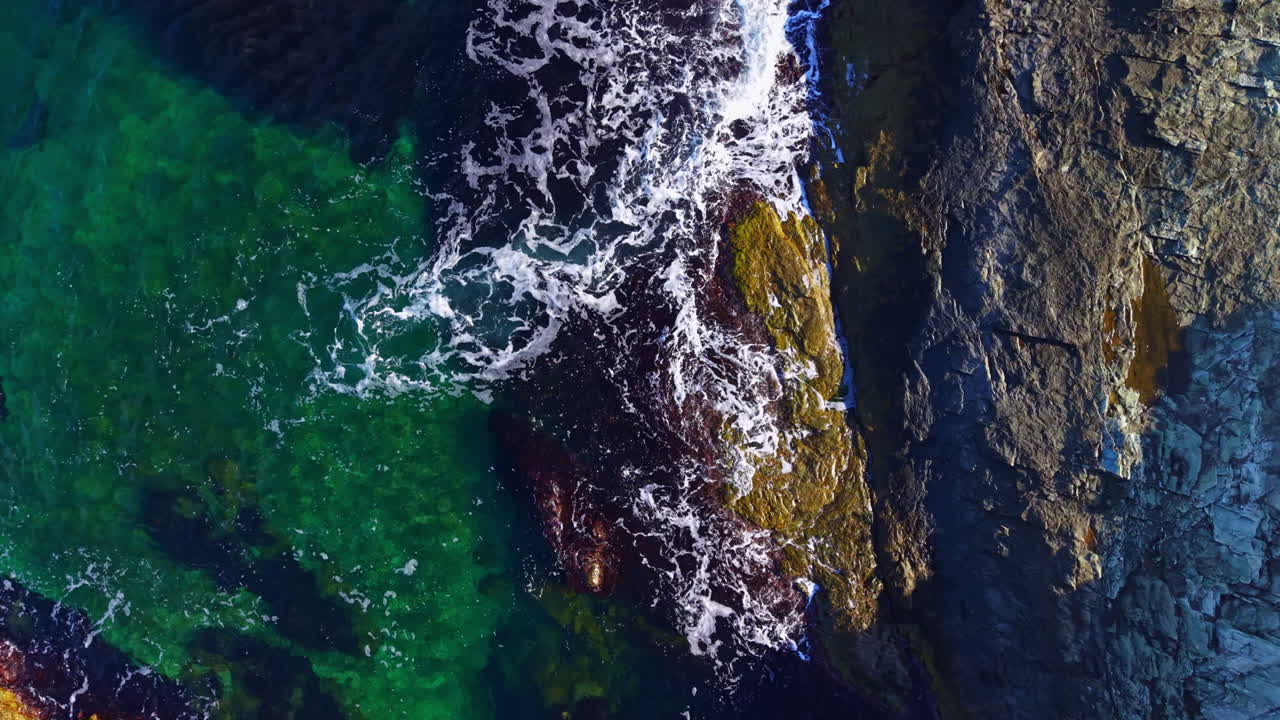 Onde che si infrangono sulla costa rocciosa mentre la luce del sole danza su acque cristalline in una tranquilla scena costiera