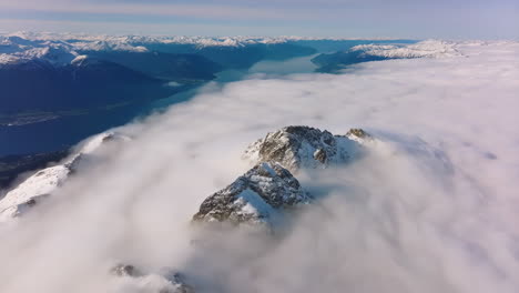 snow-capped mountain peaks emerging through a sea of clouds with a fjord in the background