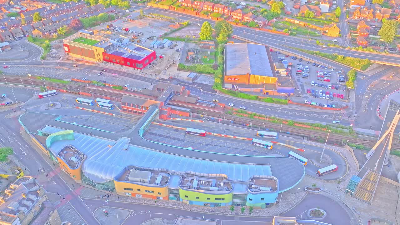 Top-down drone view of Barnsley Interchange showing curved glass-roofed bus terminal, multiple buses in service bays, surrounding roads, car parks, and retail construction sites
