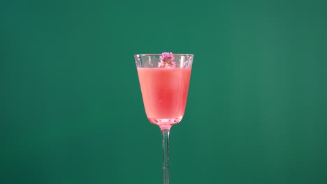 a pink cocktail is garnished with flowers using tongs against a green screen backdrop, highlighting vibrant colors and precise movements