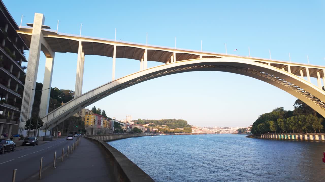 A boat sails down the Douro River with a view of the Arrábida Bridge at sunset in Porto