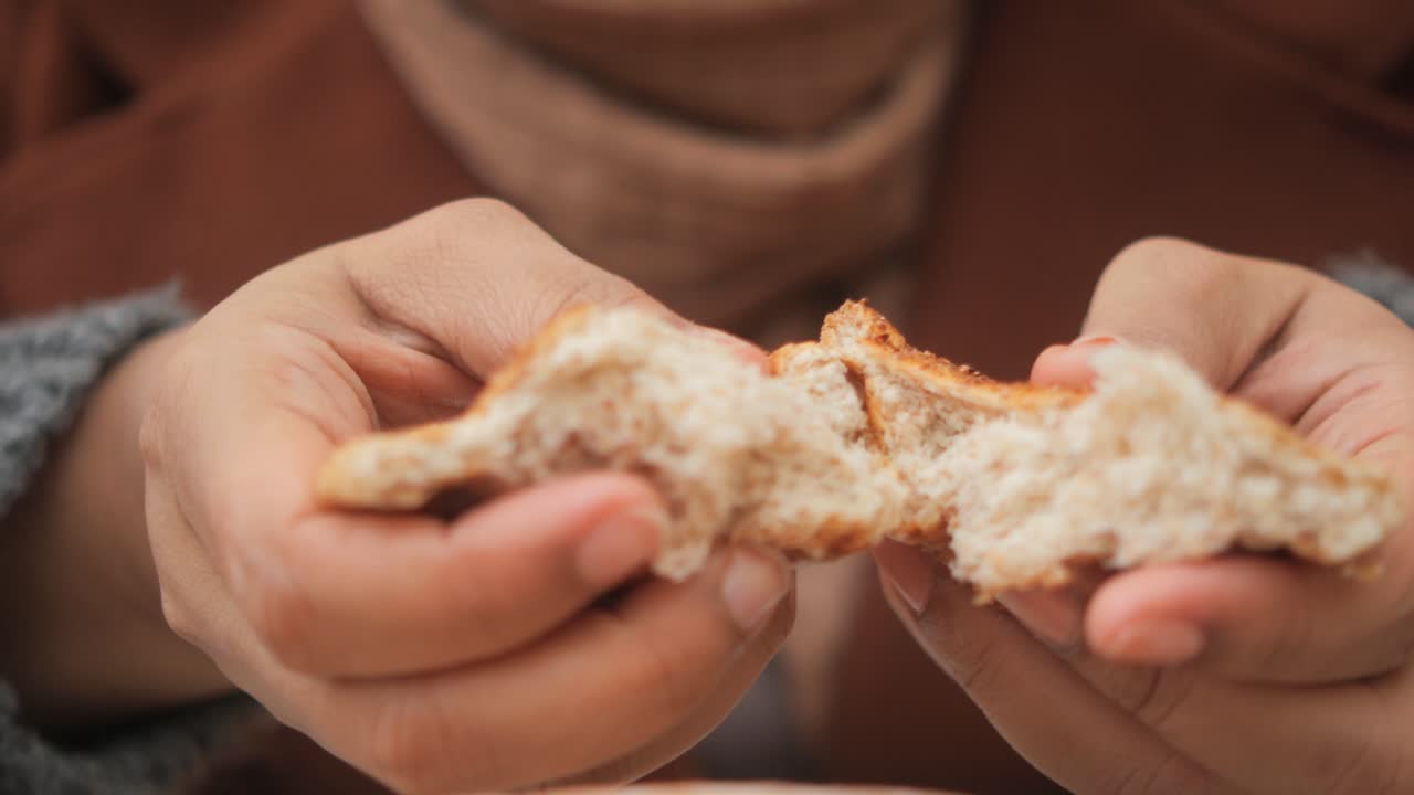 cerca de las manos de una mujer rompiendo un pedazo de pan
