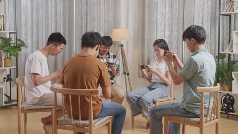 아시아 청소년 그룹이 의자에 앉아서 집에서 스마트폰으로 게임을 하고 있습니다.
