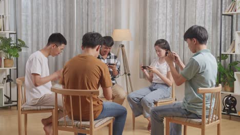 asian teen group sitting in chairs forming a circle playing game on smartphone at home