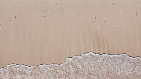 aerial view waves break on white sand beach