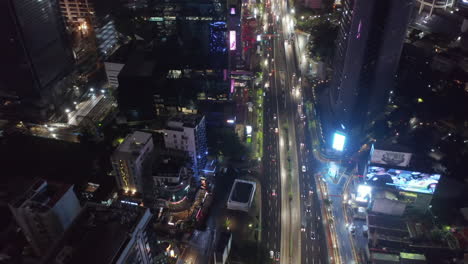 Toma-Aérea-Inclinada-Que-Volaba-Hacia-Los-Autos-En-Una-Autopista-Por-La-Noche-En-El-Ajetreado-Centro-Urbano-Metropolitano-De-Yakarta