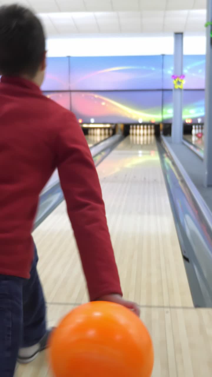 Orange bowling ball rolling down the lane towards the pins in a vibrant bowling alley with colorful lights and polished wooden floor