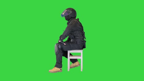 policeman wearing face mask and high tech helmet sitting waiting, thinking on a green screen, chroma key