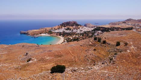 descending drone footage atop the mountains of lindos in greece looking down on the beach and the mediterranean sea with the acropolis of the city in the background