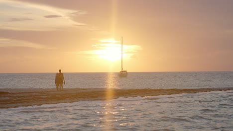 happy honeymoon couple on beach watching picturesque sunset above tropical sea and lonely sailboat, full frame slow motion