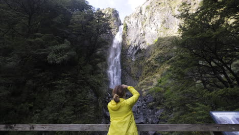 chica con chaqueta amarilla fotografiando una gran cascada en nueva zelanda