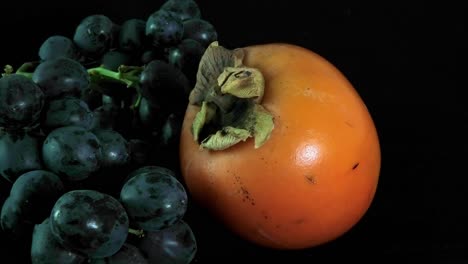 close up of persimmon with bunch of black grapes