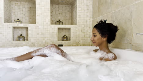 a beautiful looking indian woman spas in a bathtub with rich soap bubbles