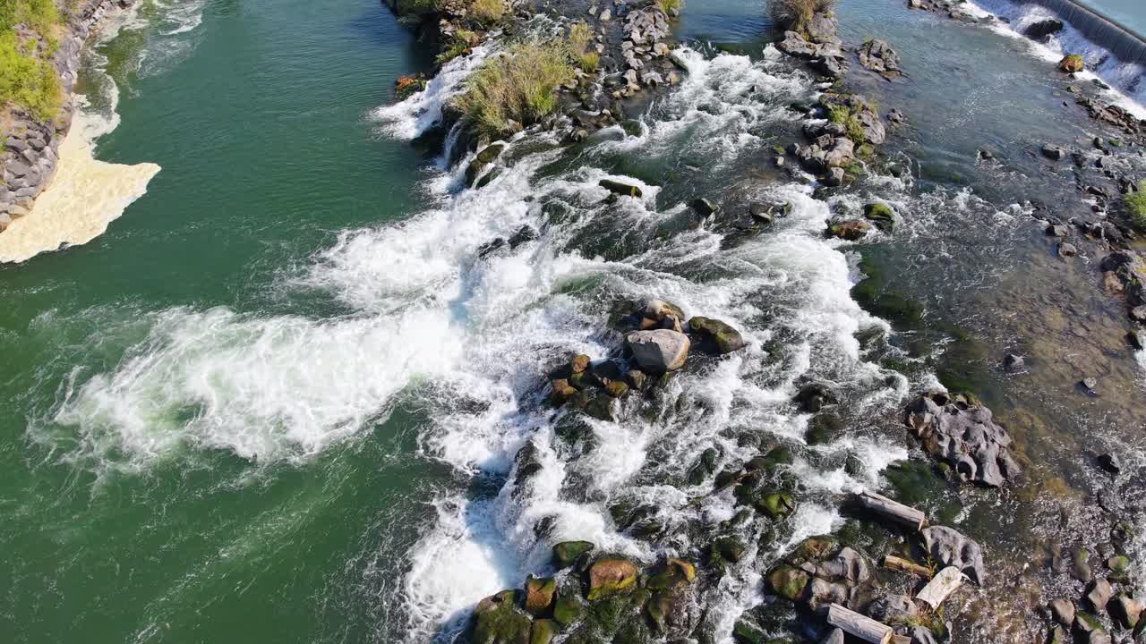 Drone footage capturing Snake River rapids crashing over rocks with nearby greenery and farmland
