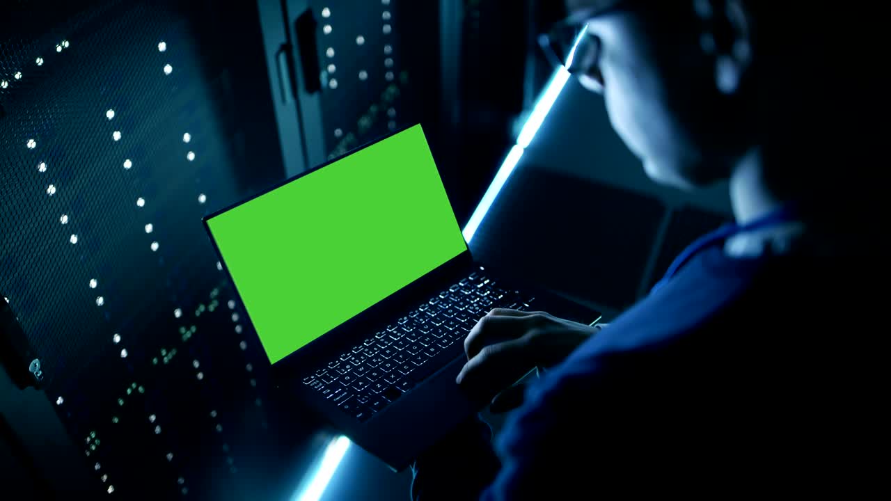 especialista sosteniendo un cuaderno con pantalla verde y trabajando en él. es empleado de un gran centro de datos ultramoderno.